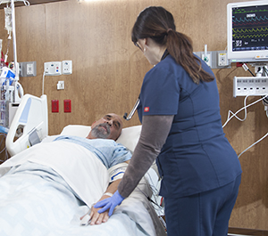 Health care provider caring for man in intensive care unit bed.