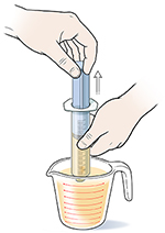 Closeup of hands drawing liquid food into syringe from measuring cup.