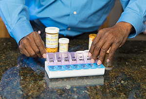 Man taking pill out of pill organizer.