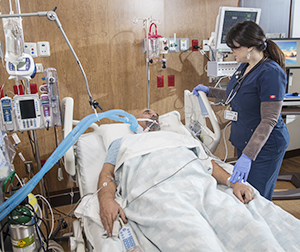 Health care provider caring for intubated man in intensive care unit bed.
