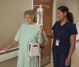 Health care provider walking with woman in hospital hallway.
