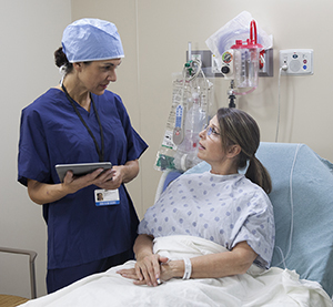 Health care provider talking to woman in pre-op hospital room.