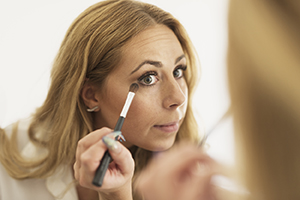 Woman looking in mirror, putting on eye makeup.