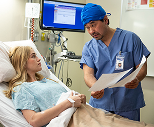 Healthcare provider showing printed materials to woman sitting up in hospital bed.