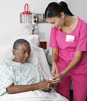 Health care provider showing PCA pump button to woman sitting up in hospital bed.