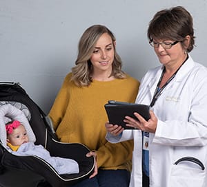 Female with baby in carrier talking to health care provider.