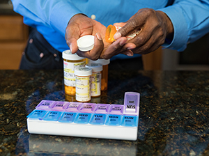 Closeup of man's hands filling pill organizer with medications.