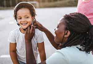 Woman putting helmet on preschooler girl on bike.