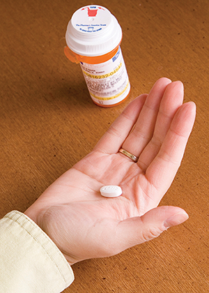 Woman’s hand holding pill with prescription pill bottle nearby.
