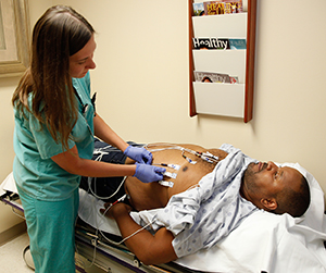 Healthcare provider performing electrocardiogram test on man in exam room.