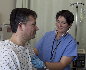 Health care provider using stethoscope on chest of man in hospital bed.