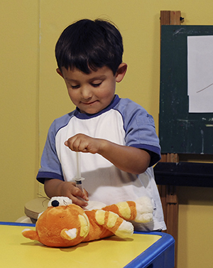 Child playing with pretend syringe and teddy bear.