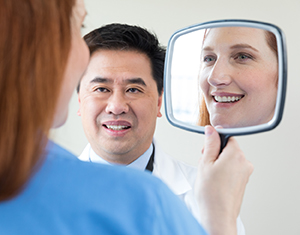 Woman looking in hand mirror with healthcare provider looking on.