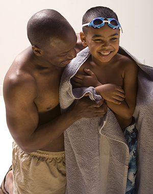 Man holding preschooler boy in towel near swimming pool.