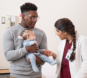 Healthcare provider talking to man with baby in exam room.