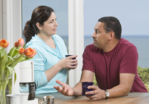 Man and woman talking over coffee at kitchen counter. 