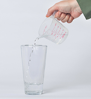 Hand pouring water from measuring cup into drinking glass.