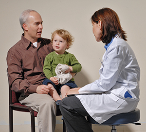 Boy sitting on man's lap while man talks to healthcare provider.