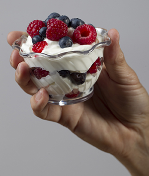 Hand holding glass dish of yogurt and fresh berries.