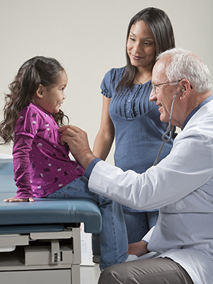 Healthcare provider listening to girl's chest with stethoscope. Woman standing nearby.