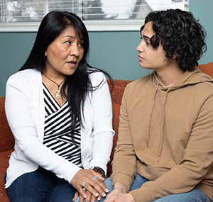 Woman and teen boy sitting on couch having serious conversation.