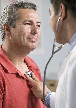 Healthcare provider listening to man's chest with stethoscope.