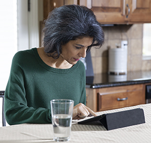 Woman sitting at table looking at electronic tablet.