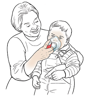 Woman holding toddler boy on lap and helping him breathe through mask with metered-dose inhaler.