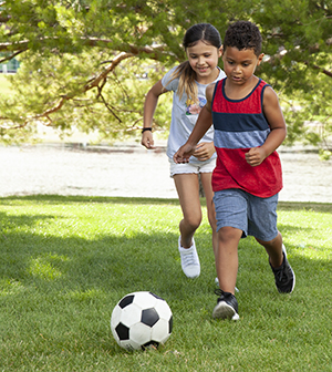 Niña y niño jugando con una pelota de fútbol.