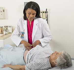 Healthcare provider examining woman's abdomen in exam room.