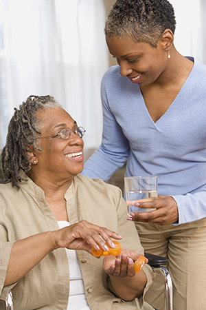 Woman handing glass of water to older woman to take her medicine.