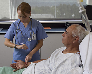 Healthcare provider checking patient’s pulse in hospital bed.