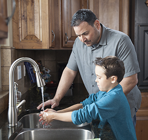 Man helping boy wash his hands in kitchen sink