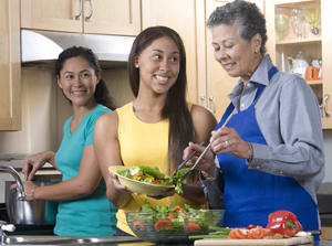 Three people in kitchen making a meal.