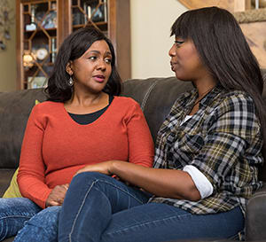 Two people sitting on couch talking.